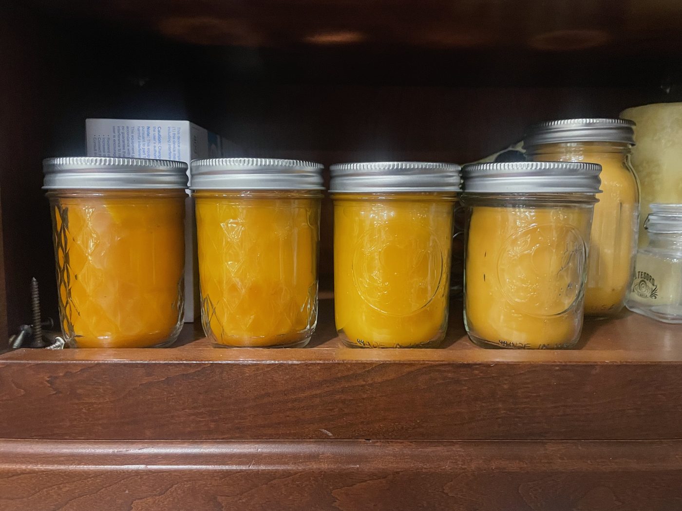 Mason jars of cured honey lined up on a wooden pantry shelf.